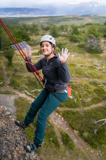 Escaladora sonriendo y saludando con las dos manos mientras la bajan por la vía, con el valle detrás
