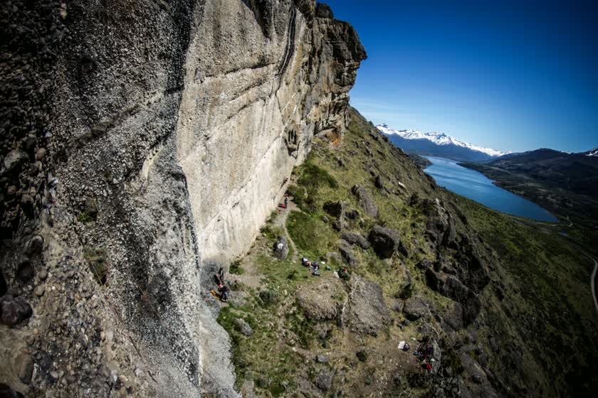 La pared del Cerro Benítez vista desde arriba, con el sendero al pie, el lago y las montañas nevadas al fondo