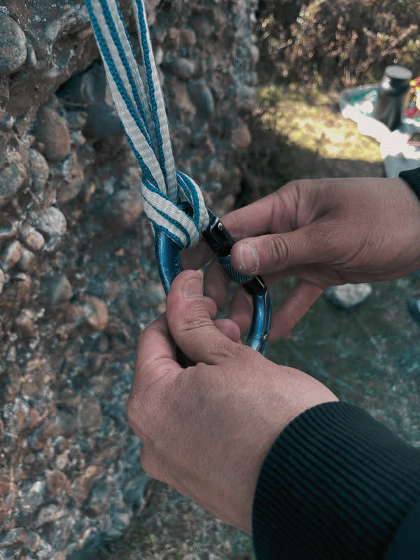 Manos uniendo una cinta a un mosquetón para montar un anclaje