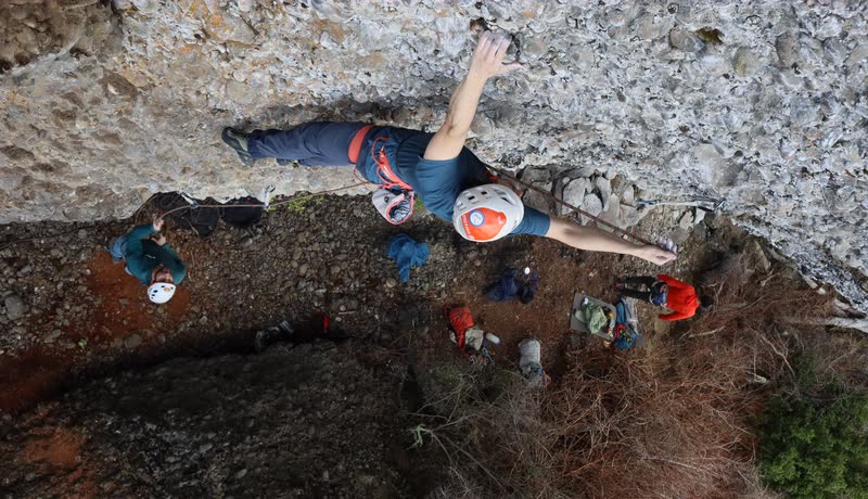 Escalador superando el techo de conglomerado visto desde arriba, con el grupo al pie de la vía